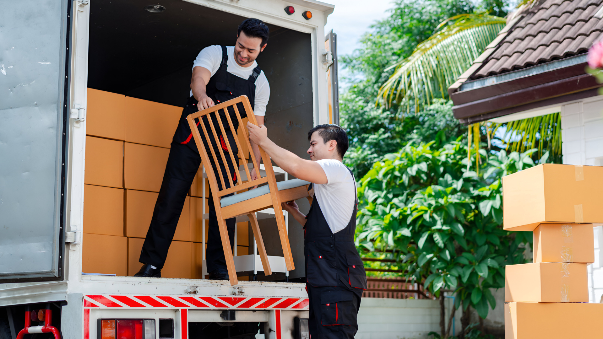 Professional movers from the best movers & packers team carefully loading a wooden chair and boxes onto a truck in a residential area with greenery in the background